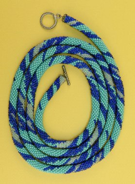 Kadın mücevherleri. Kanca kapaklı, çok renkli boncuklardan örülmüş bir kolye. Sarı arkaplanda izole edilmiş.