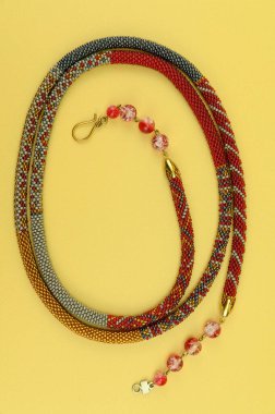 Kadın mücevherleri. Kolye, her iki ucunda süs cam boncukları olan çok renkli boncuklardan örülmüş. Sarı arkaplanda izole edilmiş.