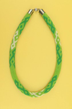 Kadın mücevherleri. Manyetik kapaklı çok renkli boncuklardan örülmüş bir kolye. Sarı arkaplanda izole edilmiş.