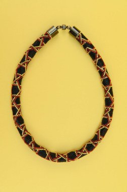 Kadın mücevherleri. Manyetik kapaklı çok renkli boncuklardan örülmüş bir kolye. Sarı arkaplanda izole edilmiş.