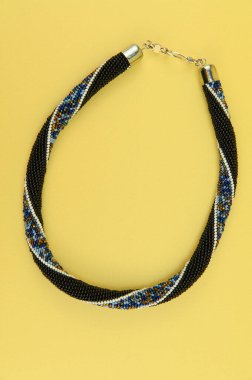 Kadın mücevherleri. Manyetik kapaklı çok renkli boncuklardan örülmüş bir kolye. Sarı arkaplanda izole edilmiş.