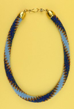 Kadın mücevherleri. Manyetik kapaklı çok renkli boncuklardan örülmüş bir kolye. Sarı arkaplanda izole edilmiş.