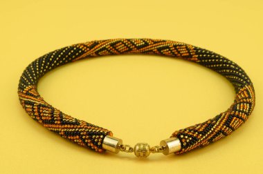 Kadın mücevherleri. Manyetik kapaklı çok renkli boncuklardan örülmüş bir kolye. Sarı arkaplanda izole edilmiş.