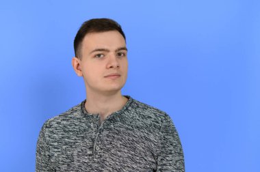 Portrait of a young attractive man who looks at the camera with a serious look. The image is made on a blue background.
