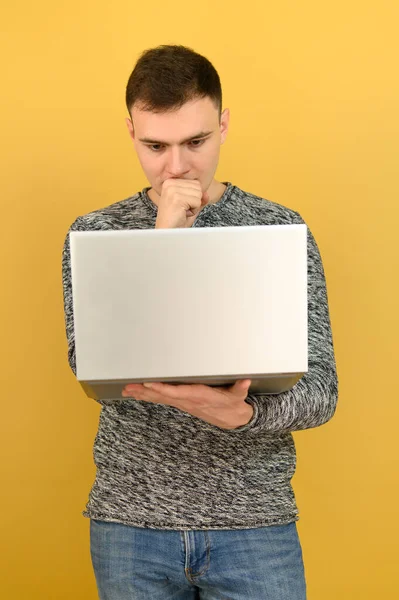 若い魅力的な男は片手でノートパソコンを保持し 普及した表情で画面を見ています 画像は黄色の背景で作成されます — ストック写真