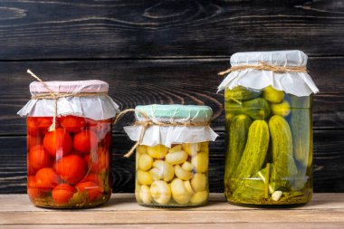 Ev yapımı kiraz domatesleri, salatalıklar, şampiyonlar, sarımsak, patlıcan, kavanozlardaki kırmızı biberler ahşap raflarda ev yapımı konserve ve mayalanmış gıda konsepti mevsimlik ürünler.