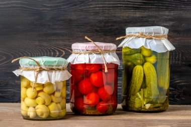 Ev yapımı kiraz domatesleri, salatalıklar, şampiyonlar, sarımsak, patlıcan, kavanozlardaki kırmızı biberler ahşap raflarda ev yapımı konserve ve mayalanmış gıda konsepti mevsimlik ürünler.