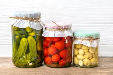 Ev yapımı kiraz domatesleri, salatalıklar, şampiyonlar, sarımsak, patlıcan, kavanozlardaki kırmızı biberler ahşap raflarda ev yapımı konserve ve mayalanmış gıda konsepti mevsimlik ürünler.