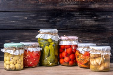 Ev yapımı kiraz domatesleri, salatalıklar, şampiyonlar, sarımsak, patlıcan, kavanozlardaki kırmızı biberler ahşap raflarda ev yapımı konserve ve mayalanmış gıda konsepti mevsimlik ürünler.