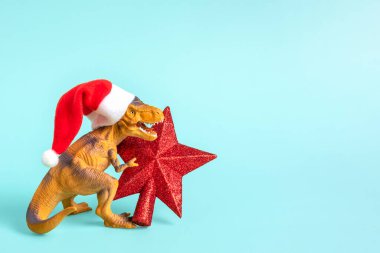 Kırmızı Noel Baba şapkalı dinozor Rex 'in mavi arka planda bir yıldızı var. Yeni yıl arifesinde ya da Noel arifesinde. Mutlu Noel' ler için yaratıcı bir fikir..