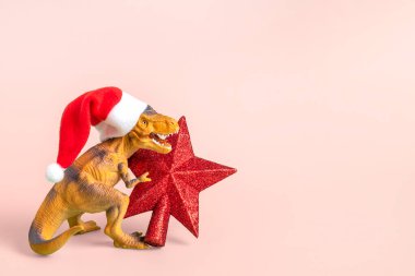 Kırmızı Noel Baba şapkalı dinozor Rex 'in pembe arka planda bir yıldızı var. Yeni yıl arifesinde veya Noel arifesinde. Mutlu Noel' ler için yaratıcı bir fikir..