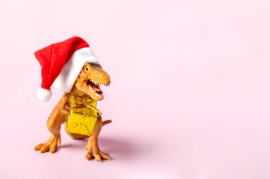 Kırmızı Noel Baba şapkalı dinozor Rex 'in pençelerinde altın hediye kutusu var. Yeni yıl arifesinde ya da Noel arifesinde. Mutlu Noeller için yaratıcı bir fikir..