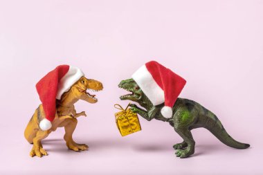 Kırmızı Noel Baba şapkalı dinozor Rex 'in pençelerinde altın hediye kutusu var. Yeni yıl arifesinde ya da Noel arifesinde. Mutlu Noeller için yaratıcı bir fikir..