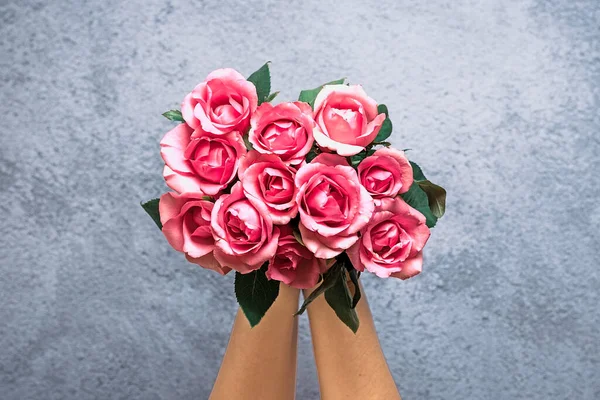 female hands hold romantic bouquet of tender pink roses on gray concrete background Holiday floral card Birthday, Wedding, Happy Valentine\'s, Mother\'s, Teacher\'s day creative concept Top view Flat lay.