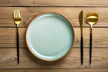 Boş yuvarlak gri tabak, çatal, bıçak, kaşık ahşap masada. Üst manzara düz tabaklar kahvaltı, öğle yemeği ya da akşam yemeği için.