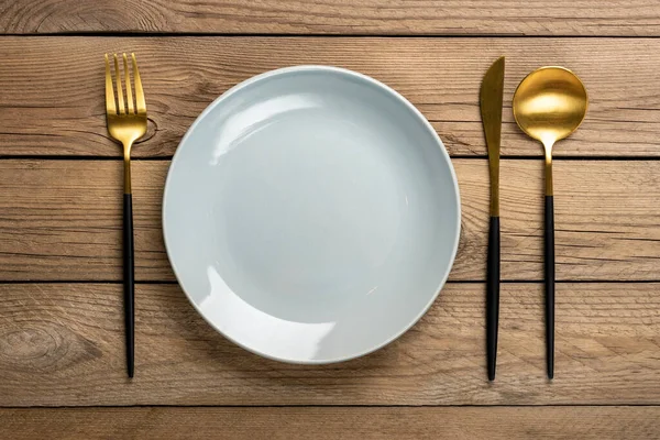 จานสีเทากลมเปล่า, ฟอร์ค, มีด, ช้อนบนโต๊ะไม้ ท็อปวิว จานวางแบนสําหรับอาหารเช้า, กลางวันหรือมื้อเย็น — ภาพถ่ายสต็อก