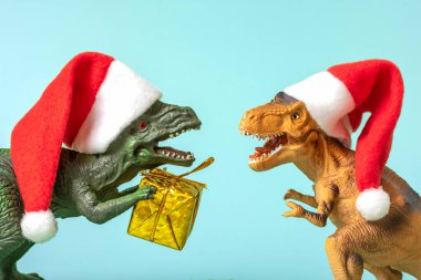 Kırmızı Noel Baba şapkalı iki dinozor Rex 'in elinde pembe arka planda altın hediye kutusu var. Yeni yıl arifesinde ya da Noel arifesinde. Mutlu Noeller için yaratıcı bir fikir..