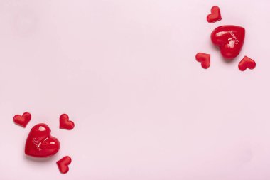 Kalp şeklinde bir çerçeve, pembe arkaplan üzerinde kırmızı kalpler düzeni. Üst görünümde düz bir tatil kartı uzanıyor. Sevgililer günün kutlu olsun, aşk konsepti..