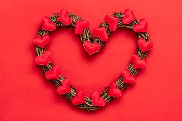 Heart shaped rattan plant wreath decorated with red hearts on red background Top view Flat lay Holiday card Happy Valentines day, love concept Copy space — Stockfoto