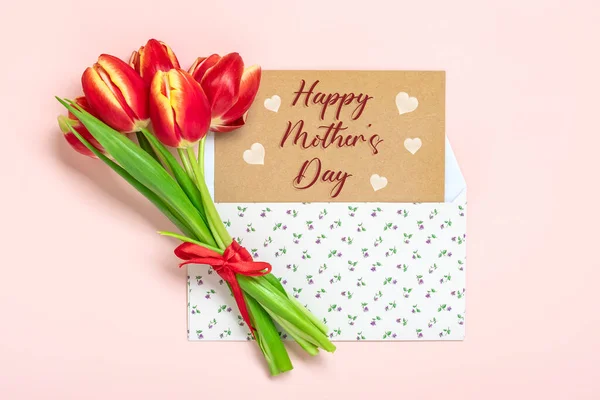 Bouquet of red tulips, text Happy Mothers Day on card in envelope on pink background Top view Flat lay Holiday greeting card