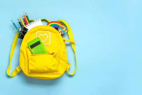 Back to school, education concept Yellow backpack with school supplies - notebook, pens, eraser rainbow, numbers isolated on blue background Top view Copy space Flat lay composition.