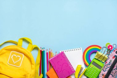 Okula dönüş, eğitim konsepti okul malzemeleriyle dolu sarı sırt çantası - not defteri, kalem, silgi gökkuşağı, mavi arkaplanda izole edilmiş numaralar Üst görünümde kopyalama alanı kompozisyonu.