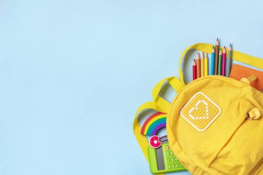 Okula dönüş, eğitim konsepti okul malzemeleriyle dolu sarı sırt çantası - not defteri, kalem, silgi gökkuşağı, mavi arkaplanda izole edilmiş numaralar Üst görünümde kopyalama alanı kompozisyonu.