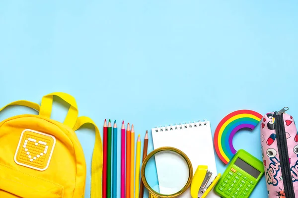 Back to school, education concept Yellow backpack with school supplies - notebook, pens, eraser rainbow, numbers isolated on blue background Top view Copy space Flat lay composition.