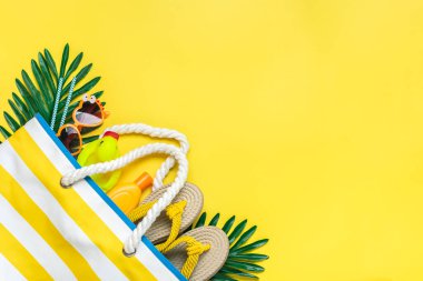 Yüzme aksesuarları - çizgili plaj çantası, güneş kremi, kalp şeklinde gözlük, sarı kaplama terliği, sarı arka planda deniz kabuğu..