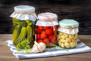 Ev yapımı kiraz domatesleri, salatalıklar, şampiyonlar, sarımsak, patlıcan, kavanozlardaki kırmızı biberler ahşap raflarda ev yapımı konserve ve mayalanmış gıda konsepti mevsimlik ürünler.