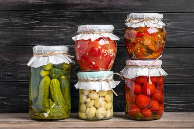 Ev yapımı kiraz domatesleri, salatalıklar, şampiyonlar, sarımsak, patlıcan, kavanozlardaki kırmızı biberler ahşap raflarda ev yapımı konserve ve mayalanmış gıda konsepti mevsimlik ürünler.
