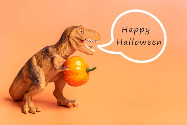 Toy dinosaur Tyrannosaurus holding pumpkin in its paws isolated on orange background Holiday greeting card Happy Halloween day, Hello Autumn creative minimal concept.