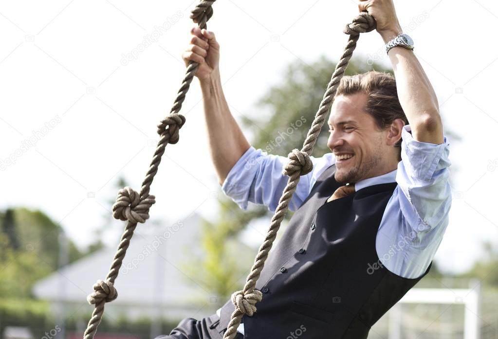 Happy businessman playing, swinging in ropes