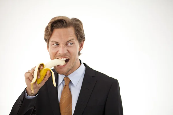 Suspicious businessman eating banana — Stock Photo, Image