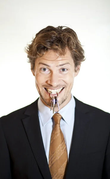 Empresário sorridente segurando chaves entre os dentes — Fotografia de Stock