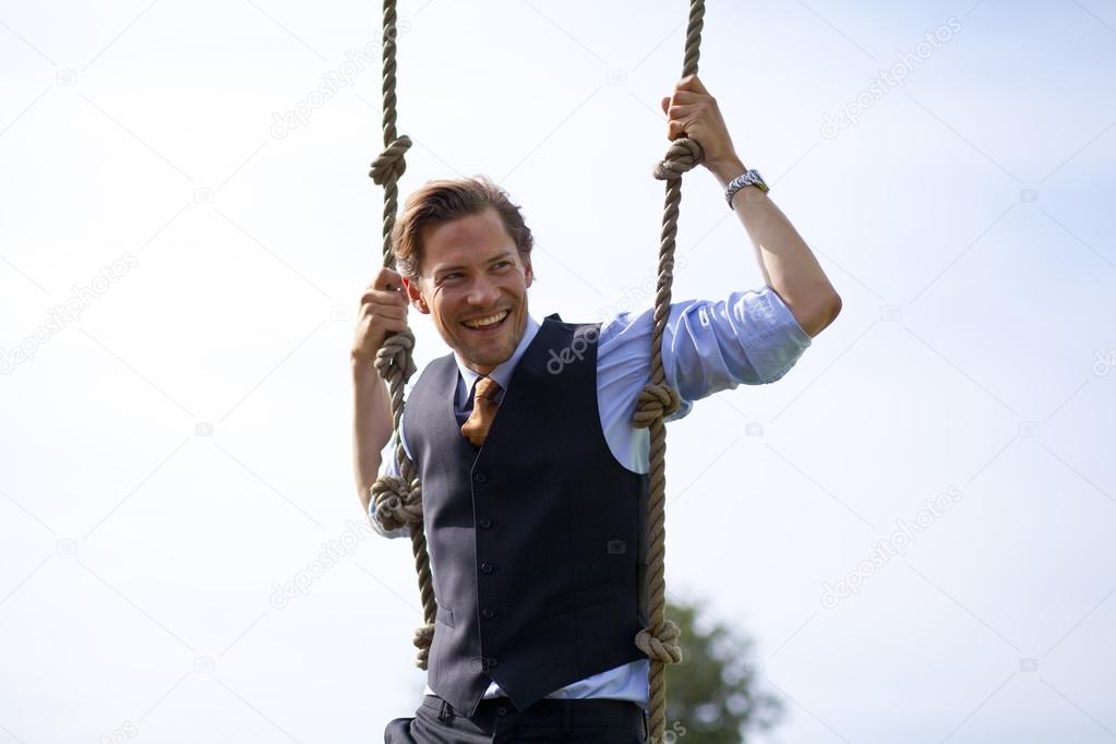 Smiling businessman swinging in ropes