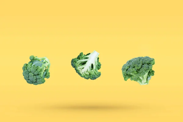 3つのブロッコリーの頭は影が付いている黄色の流行の背景で自由に落ちる 創造的な飛行食品の概念 テキストのための無料のコピースペースと最小限の野菜の背景 — ストック写真