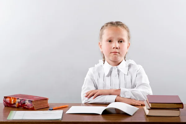 En liten skolflicka sitter vid skolan skrivbord — Stockfoto