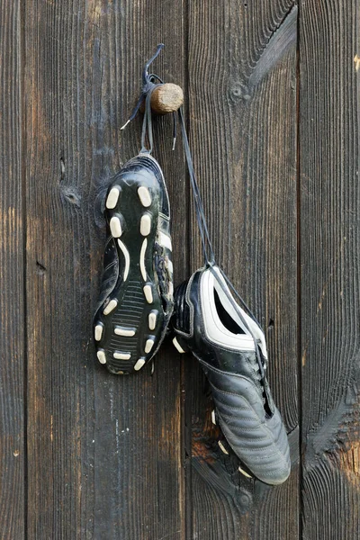 A pair of soccer boots hanging on a wooden wall. The end of the football career