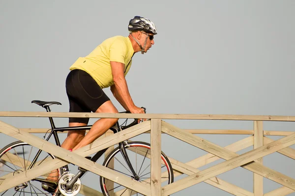 Strong middleaged man riding a bicycle over a wooden bridge at the seaside with the fresh air — Stock Photo, Image