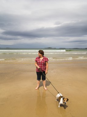 Lady walking dog on beach clipart