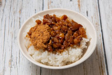 Pirinçte haşlanmış domuz eti, pilavın üstünde turşu ile servis edilir.,