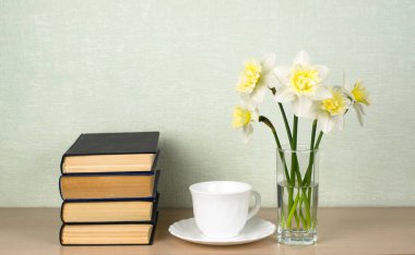 Cam vazoda bir buket hafif nergis, koyu kapaklı kalın kitaplar, beyaz bir kupa. Okuma konsepti, modern ve klasik edebiyat. Metin için yer