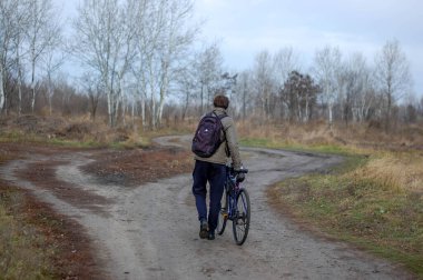Bulutlu bir sonbahar gününde sırt çantalı, kır yolunda bisikletli bir adam.