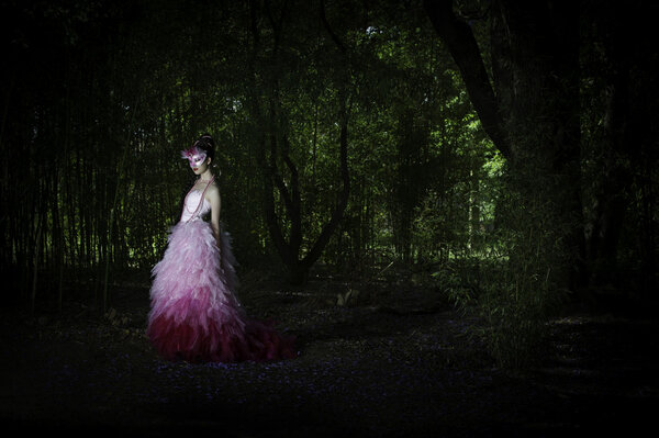 Beautiful fantasy woman standing in an enchanted dark forest, wearing her dark hair in an elaborate braided hairstyle with a pink couture evening dress