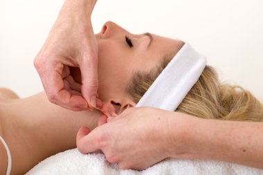 Homeopath applying an acupuncture needle on ear. clipart