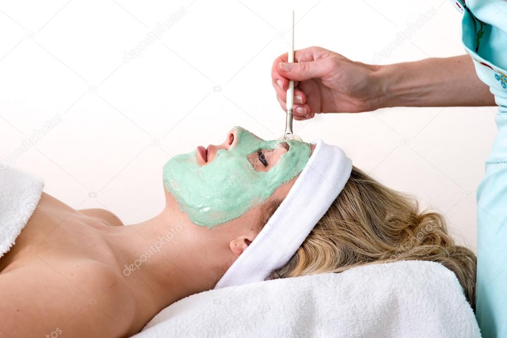 Beautician applying green facial mask on a woman.