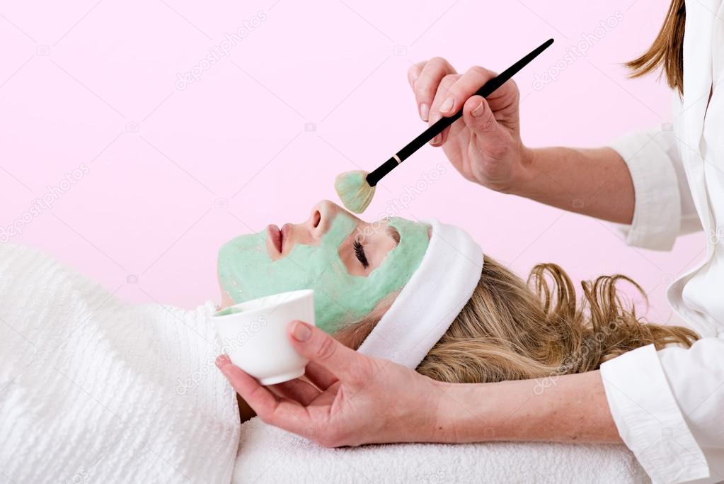Beautician brushing green facial mask on a woman.