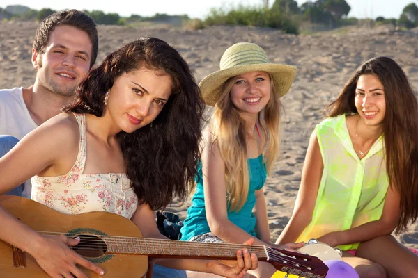 Couple and two female friends sitting on the beach playing guita — Stock Photo, Image