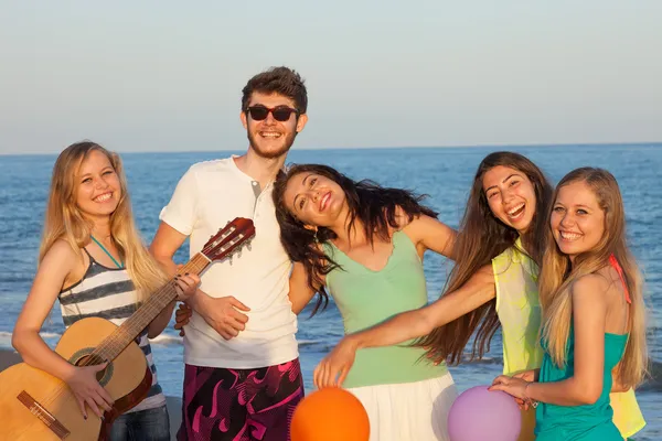 Grupo de jóvenes disfrutando de una fiesta en la playa tocando la guitarra Fotos De Stock